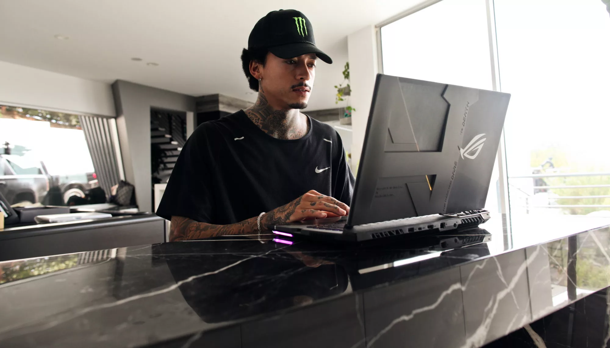 Nyjah Huston sitting at a countertop, with the custom lid of his ROG Strix laptop visible.