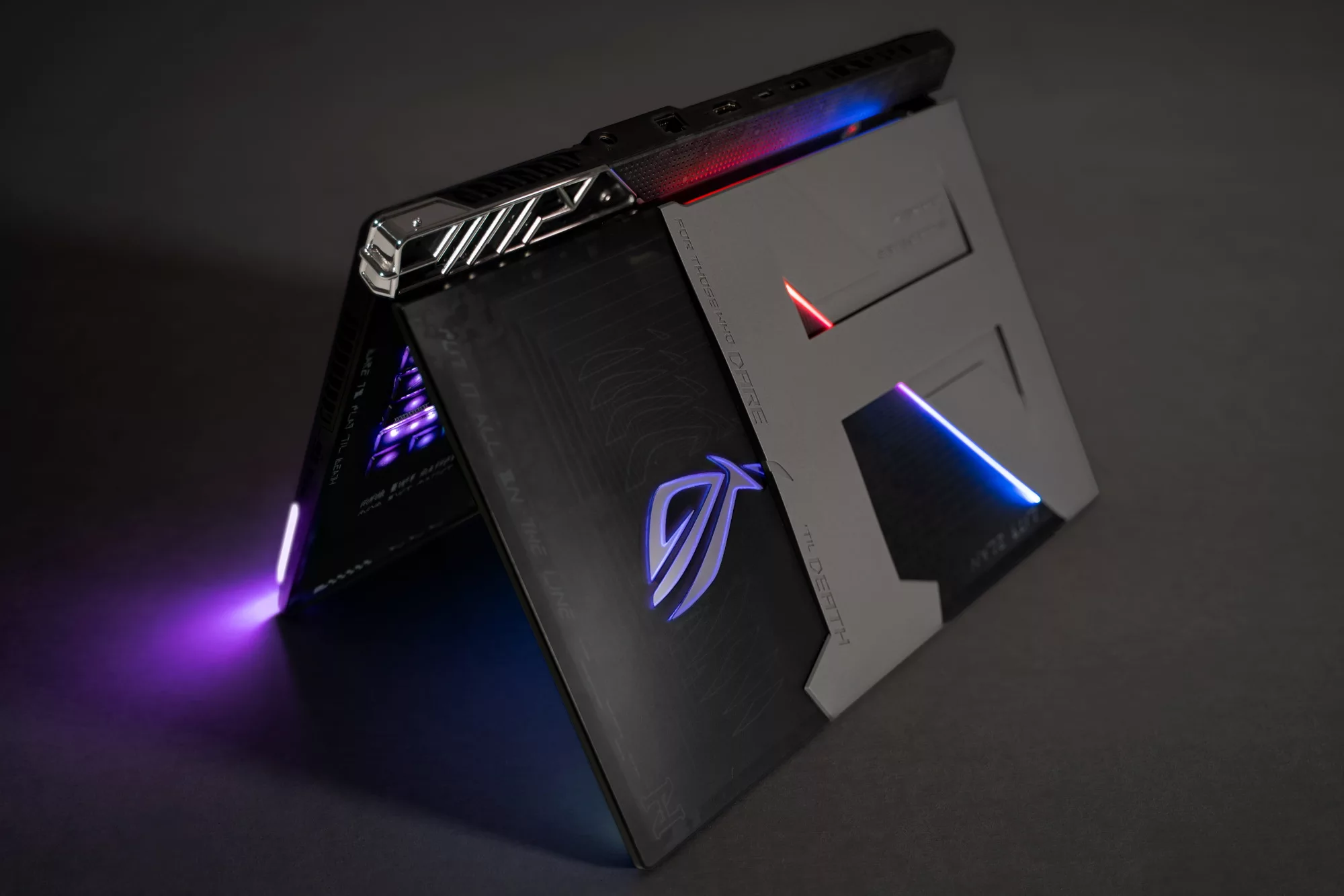The custom laptop is stood up like a tent, with purple RGB illuminated and the lid visible.