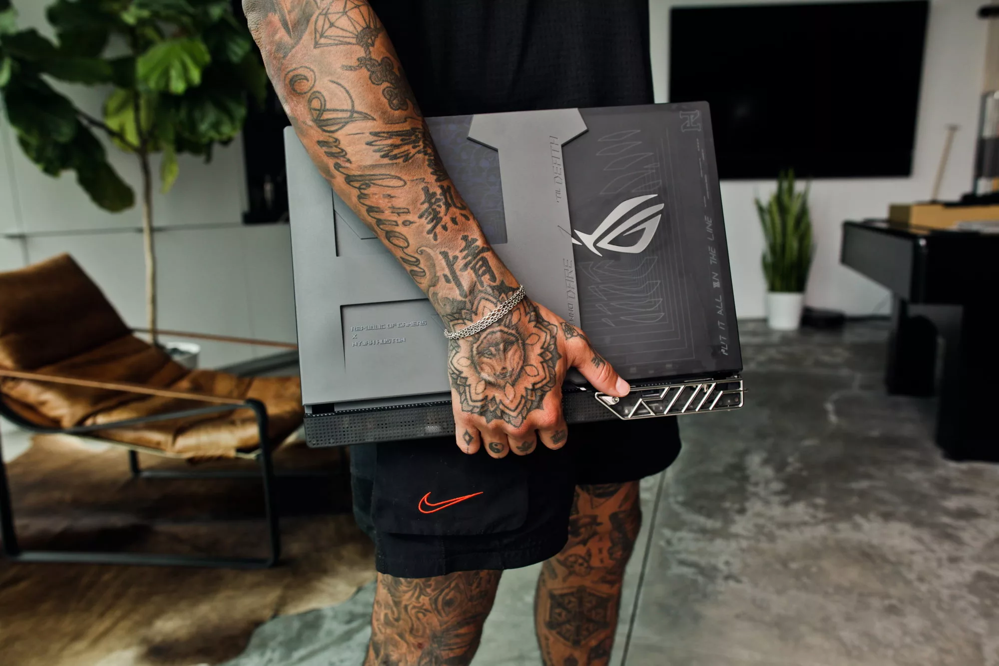 Nyjah Huston holding his laptop, with arm tattoos and the laptop lid visible.
