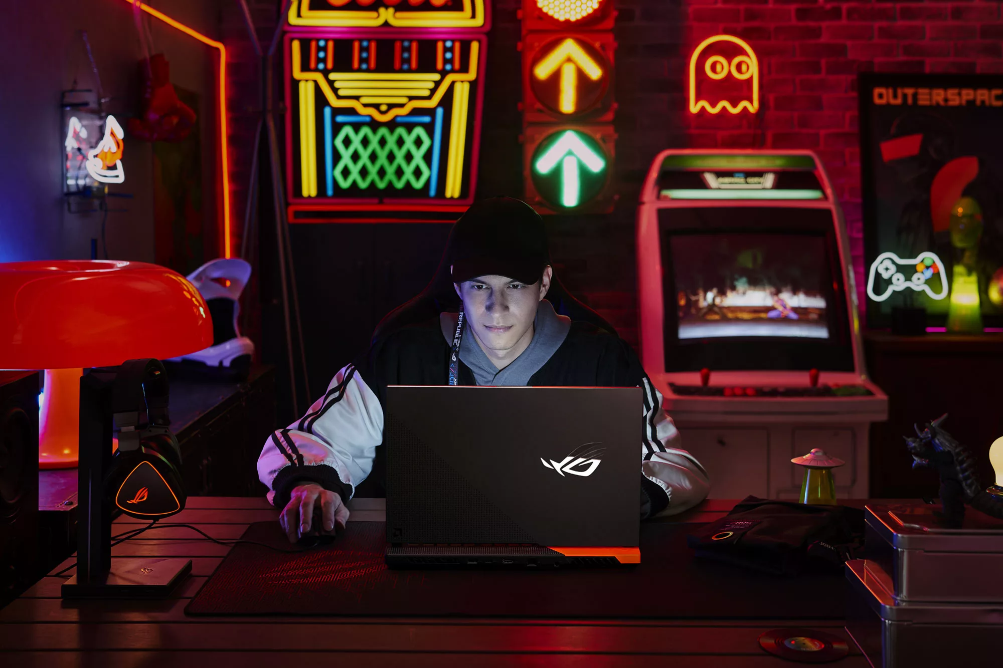 Gamer sitting in a classic video game themed room, using the ROG Strix G Advantage Edition, with a mouse and headset on the table.