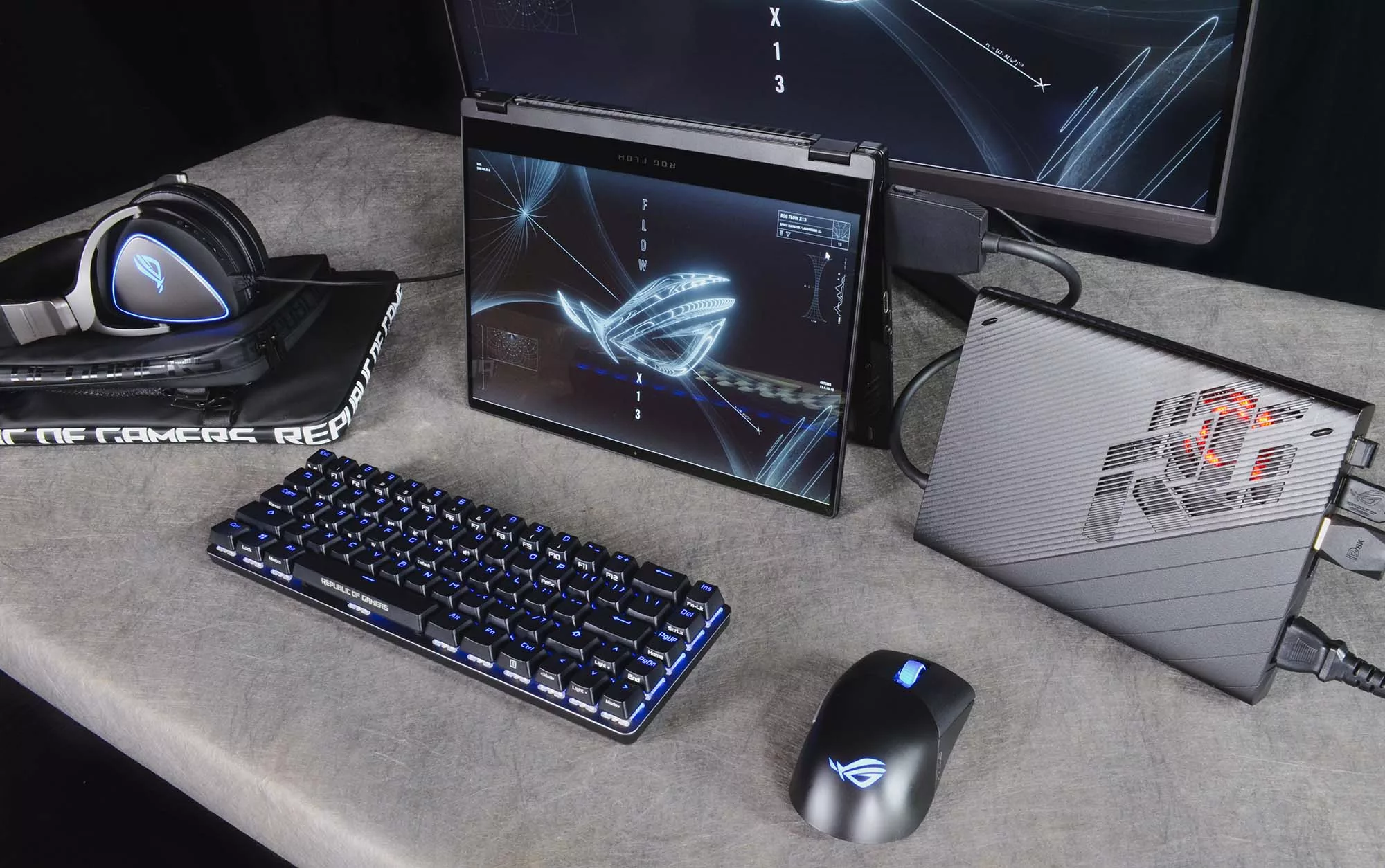 ROG Flow X13 in tent mode, connected to an XG Mobile on a table, with a secondary display, mouse, keyboard, and headset nearby.