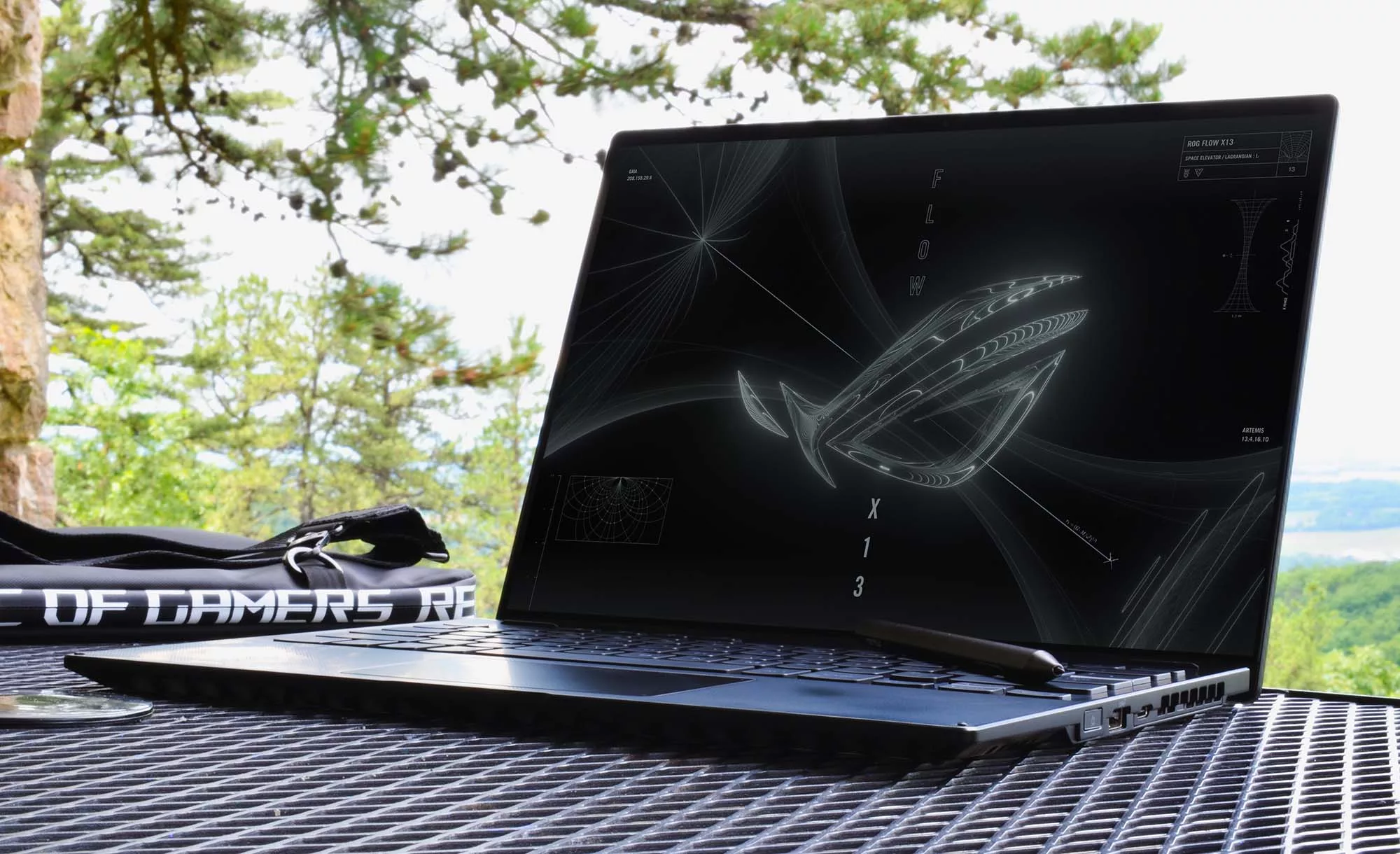 Flow X13 open with the ROG eye logo on display, with a forest in the background.