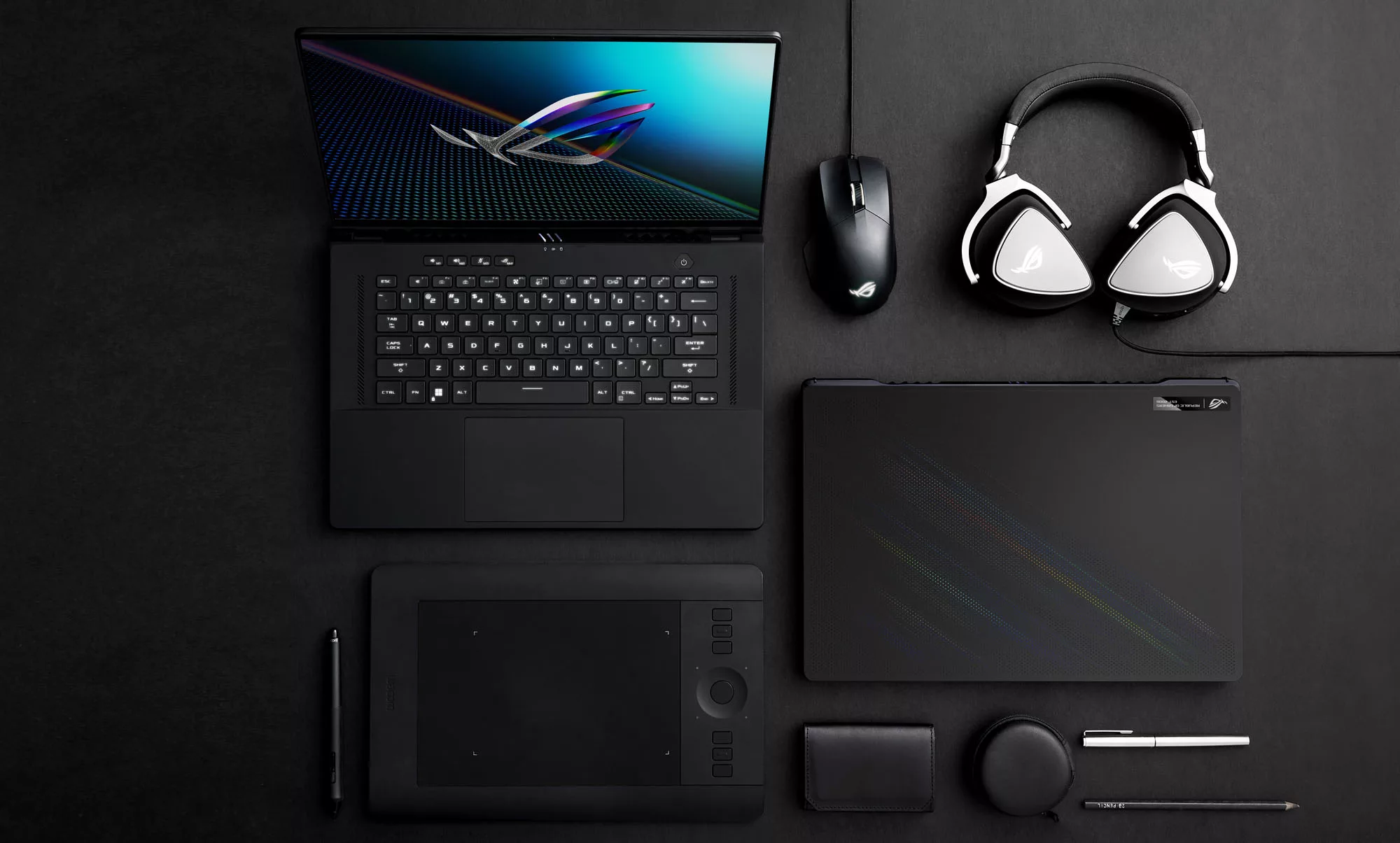 Фотографія ноутбука Zephyrus M16, оточеного периферійними пристроями, на чорному столі.