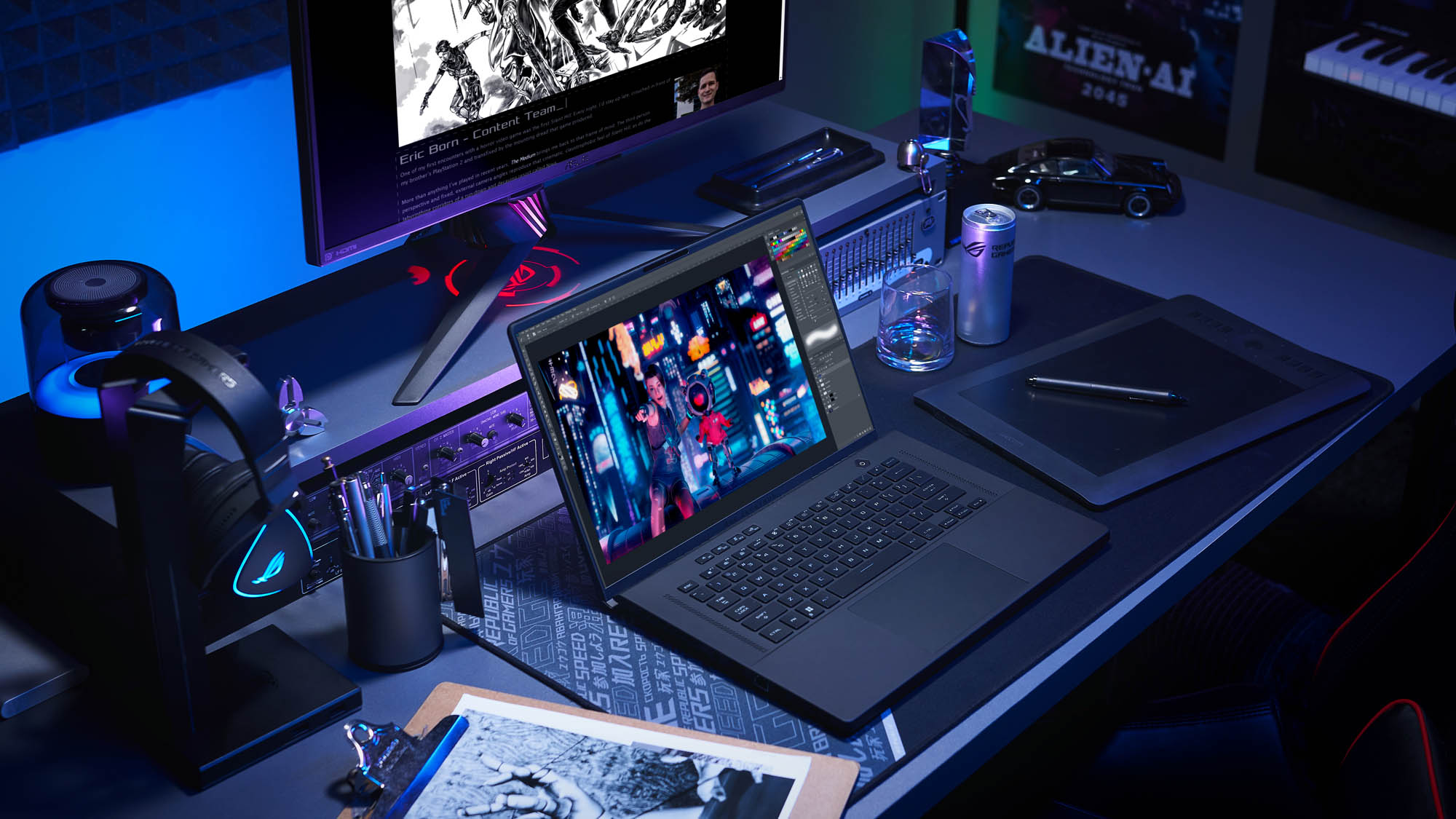 A photo of the Zephyrus M16 laptop on a desk, surrounded by drawings and other creative gear.