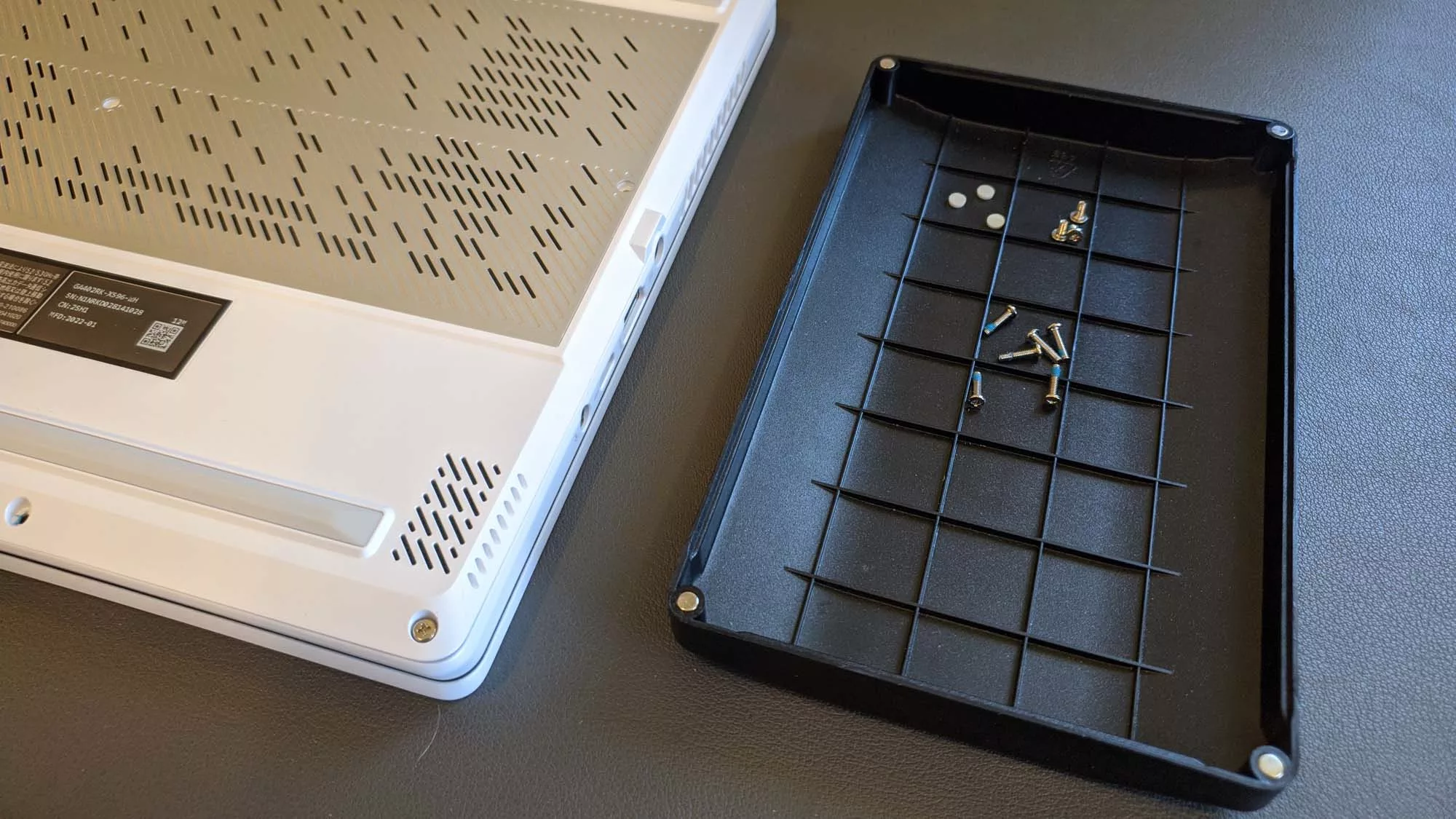 A photo of the Zephyrus G14 laptop next to a tray with many tiny screws inside.
