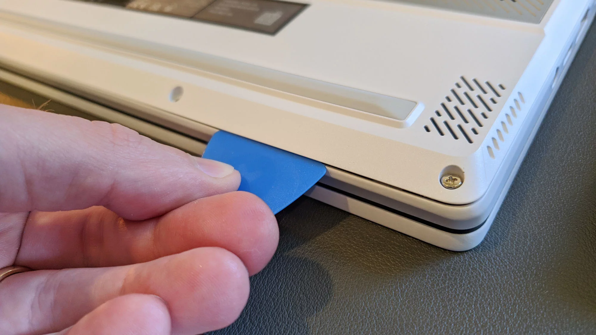 A photo of a hand inserting a guitar pick in between the panels of the Zephyrus G14 laptop.