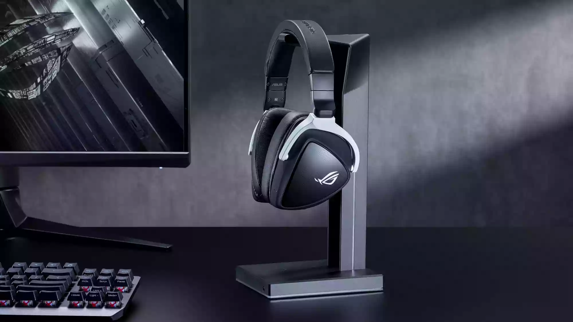 A photo of the ROG Delta S Wireless headset hanging on a headphone hook next to a gaming PC.