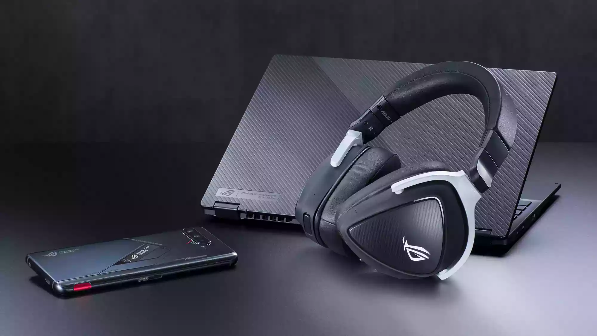 A photo of the ROG Delta S Wireless headset lying next to an ROG Flow X13 laptop and ROG Phone.