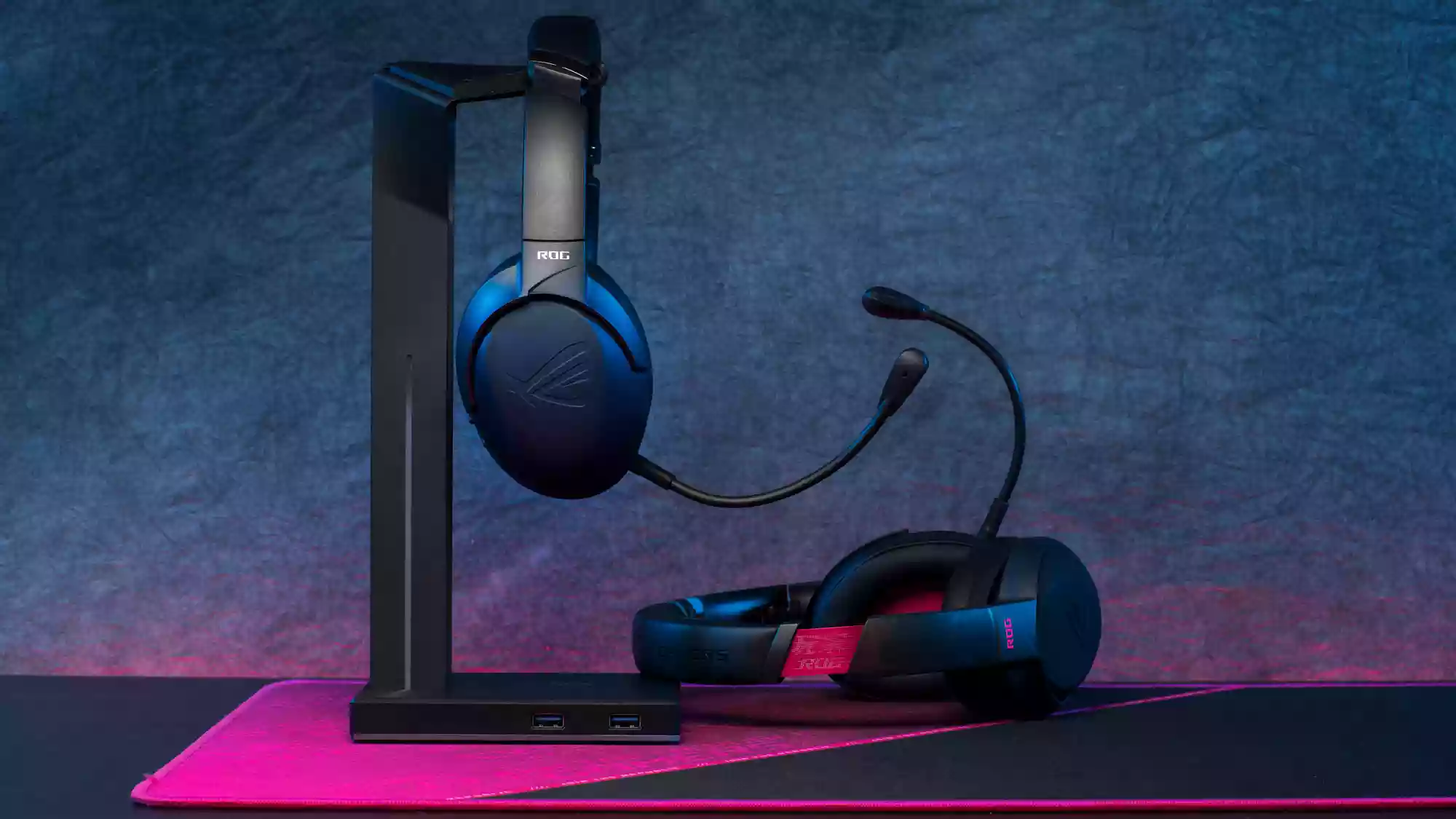 Two ROG Strix Go headsets, one resting on a desk and the other hanging on a stand.