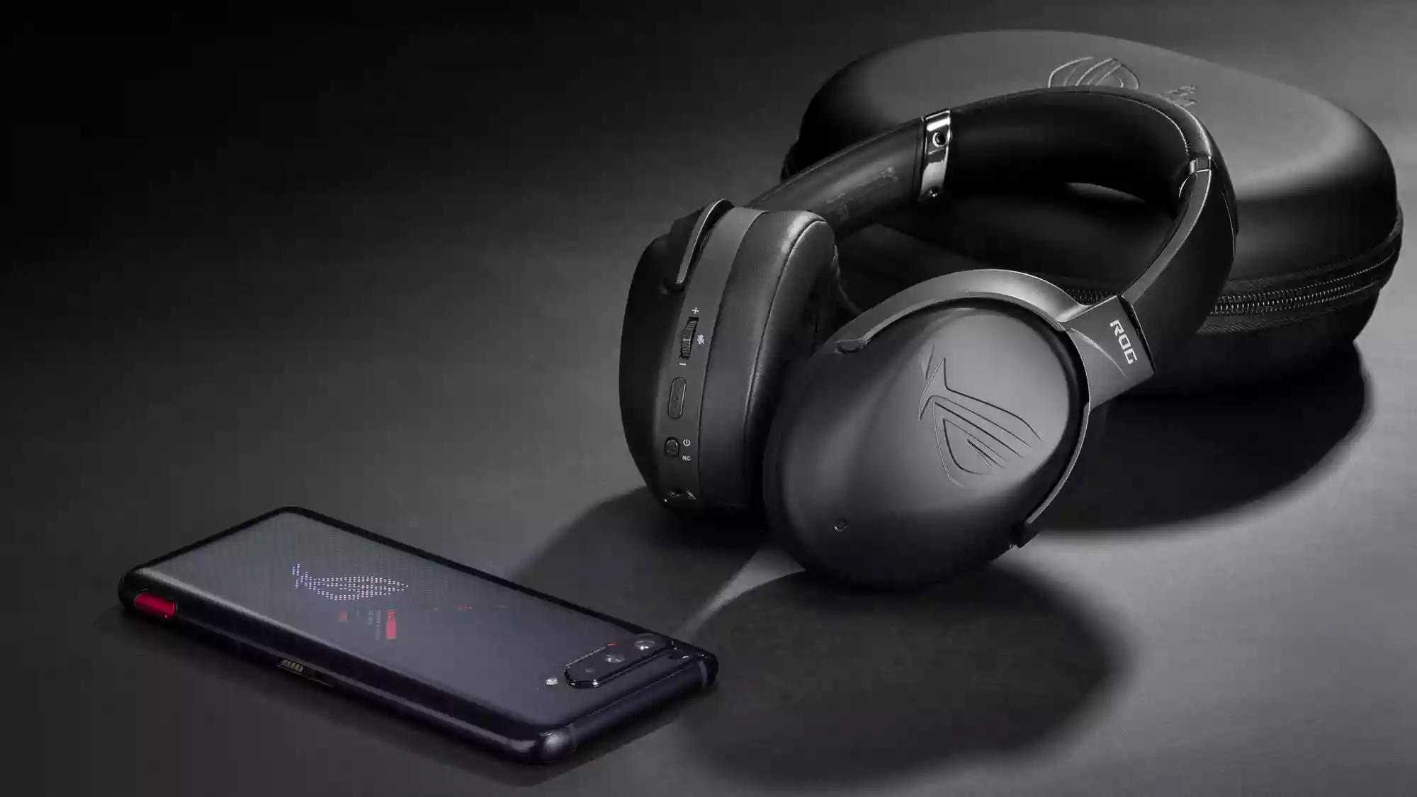 An ROG Strix Go BT headset resting on its carrying case, next to an ROG Phone on a desk.