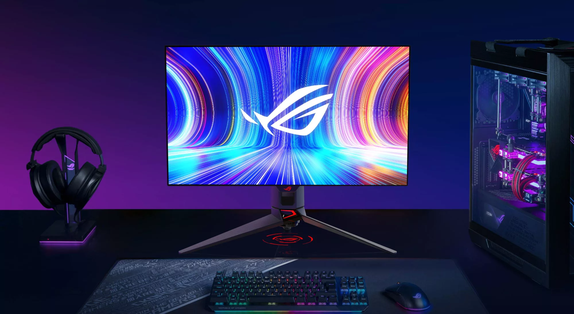 The ROG Swift OLED PG27AQDM monitor on a desk with a keyboard, headset, and desktop PC.