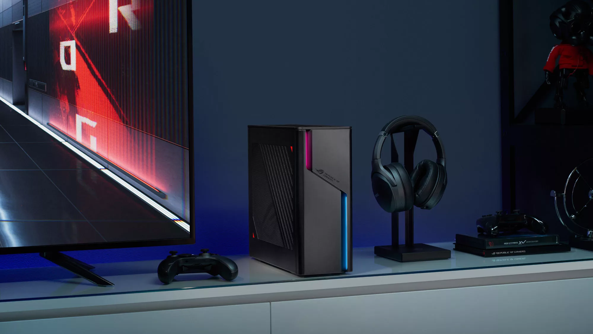 The ROG G22 desktop on an entertainment console next to a TV, gamepad, and headset.