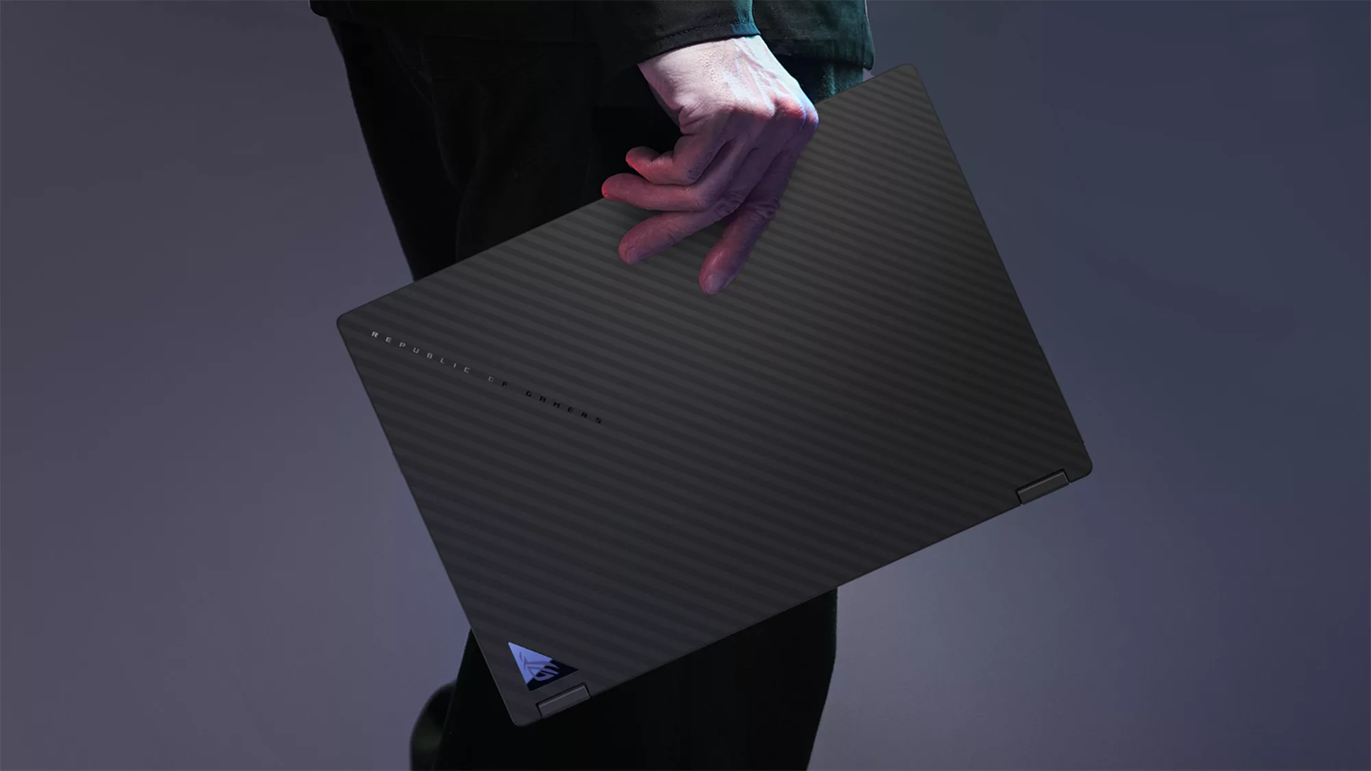 A man standing and holding a closed ROG Flow X13 laptop in his hand.