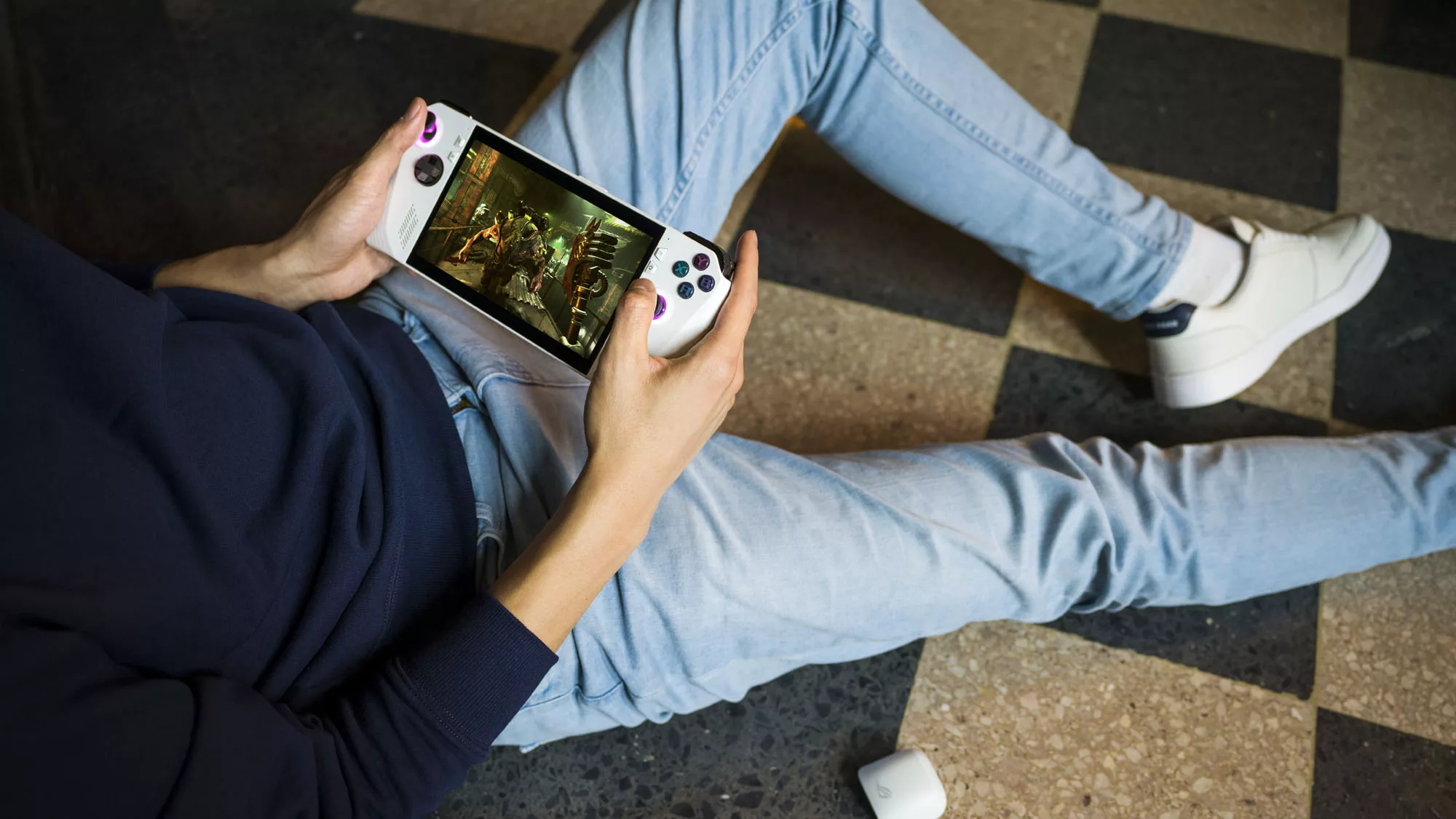 A man lying on the floor with the ROG Ally game console in his hands.
