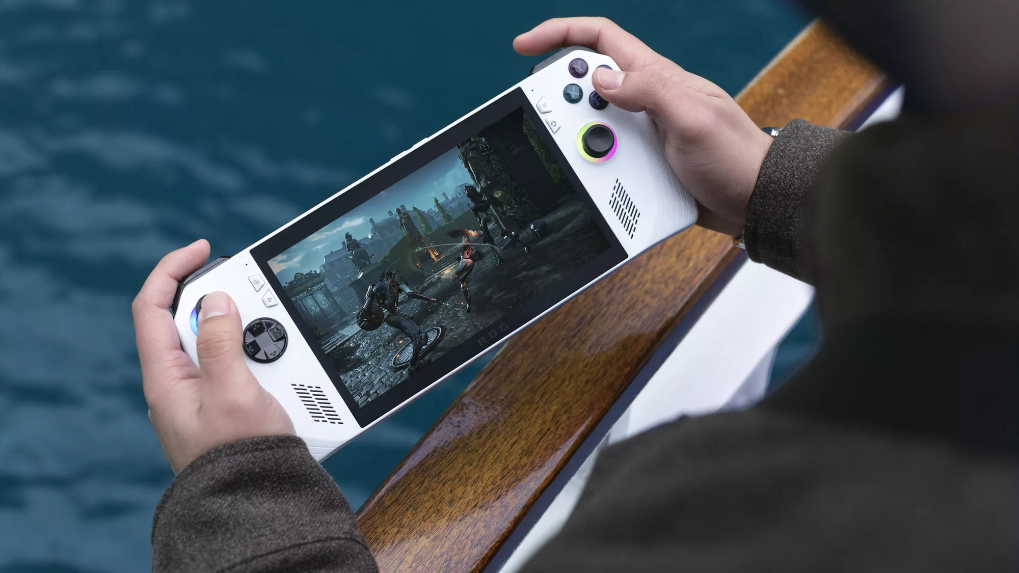 Two hands holding an ROG Ally game system on the edge of a boat over the water.
