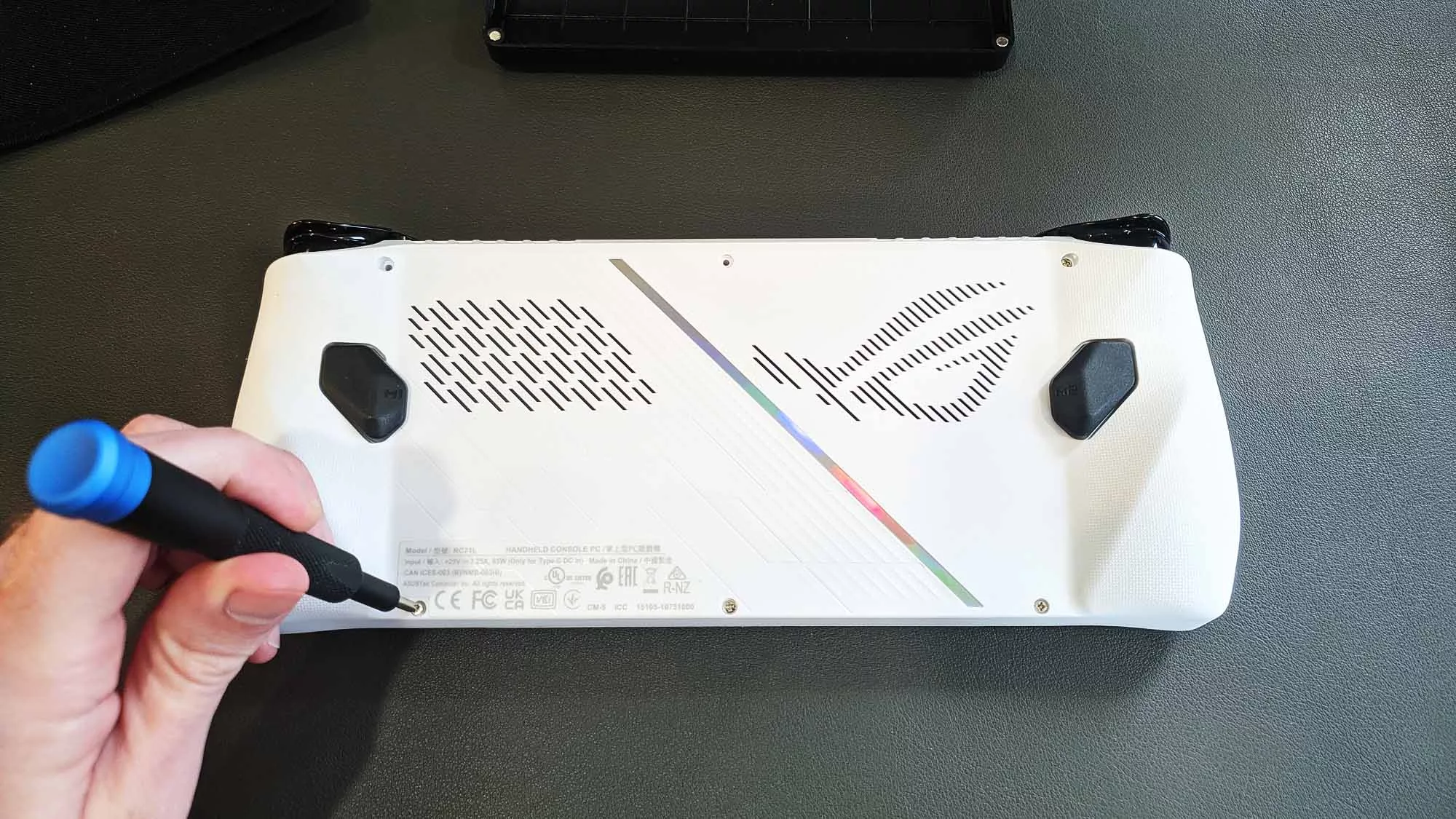 The back side of the ROG Ally, with a hand unscrewing one screw.