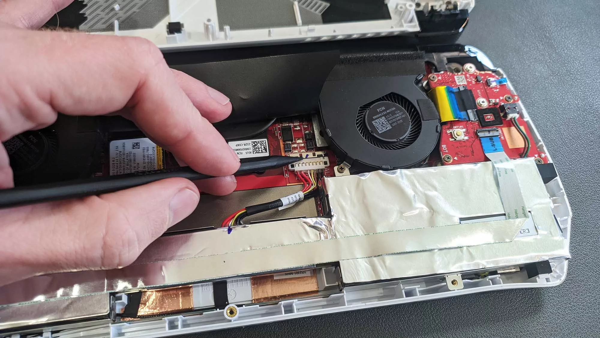 A hand using a spudger to undo the battery retaining clip inside the ROG Ally.